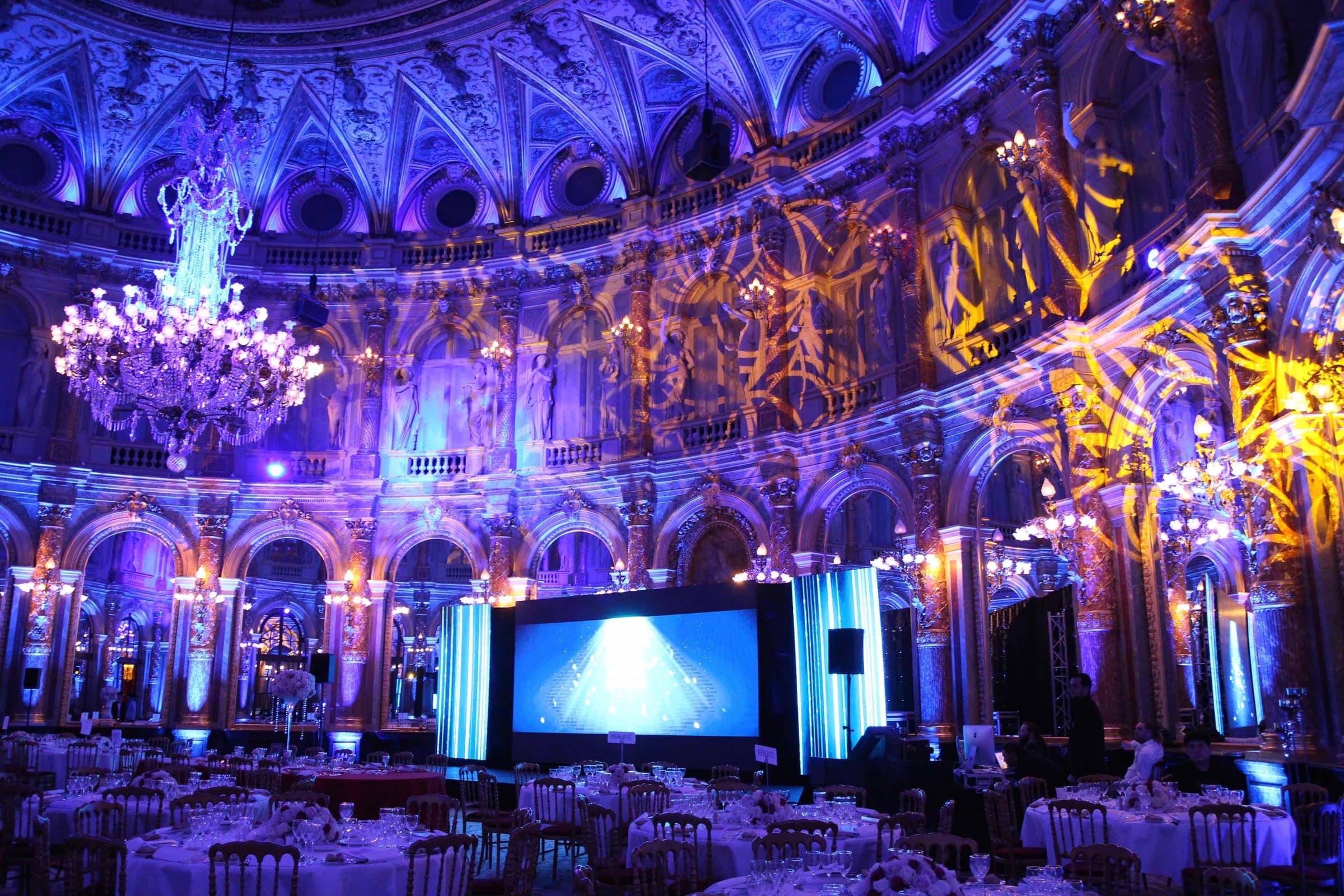 Dîner de gala dans une salle de bal historique mise en lumière, avec écran