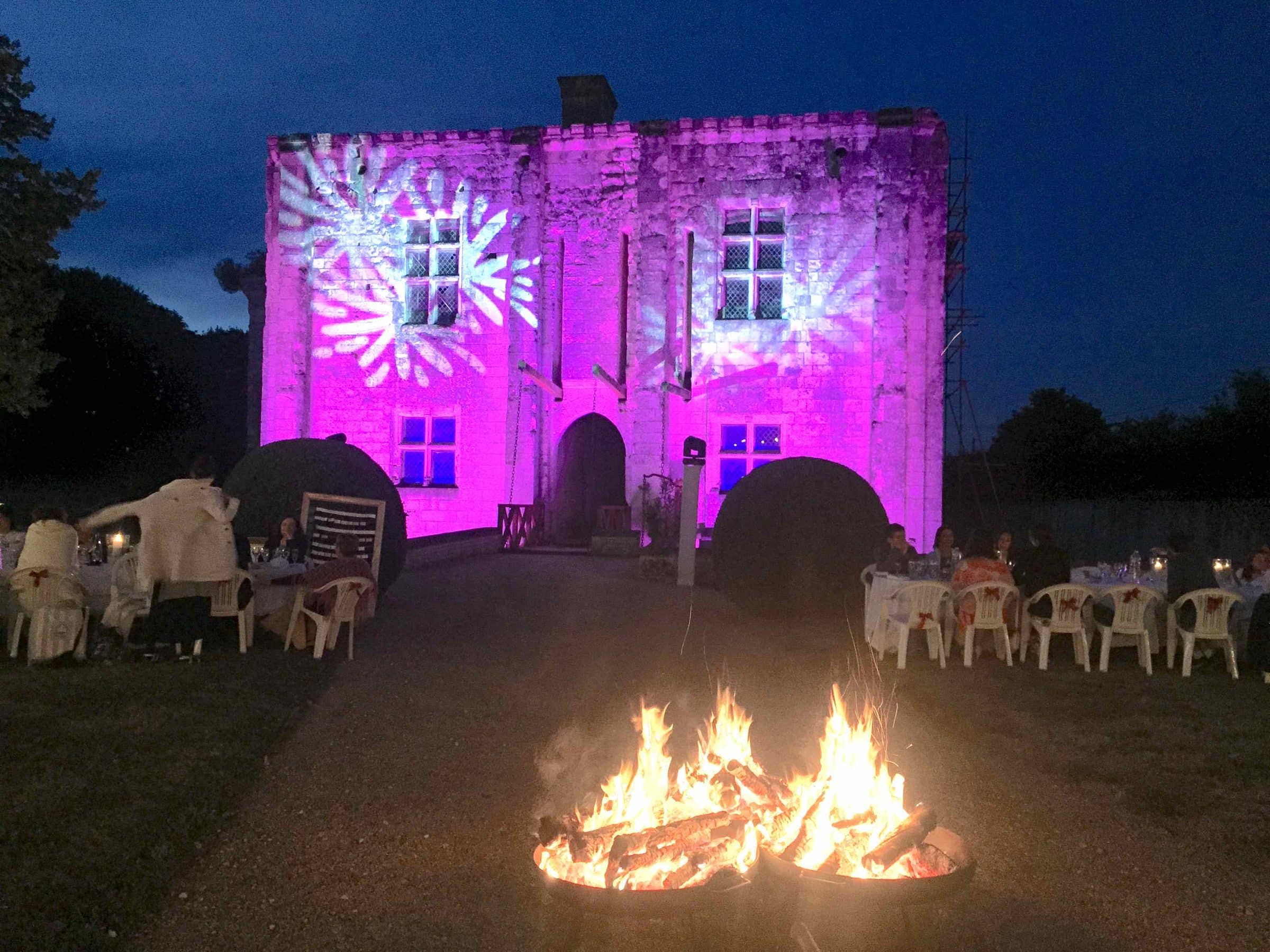 Château illuminé en rose à la nuit tombée, braséro au premier plan
