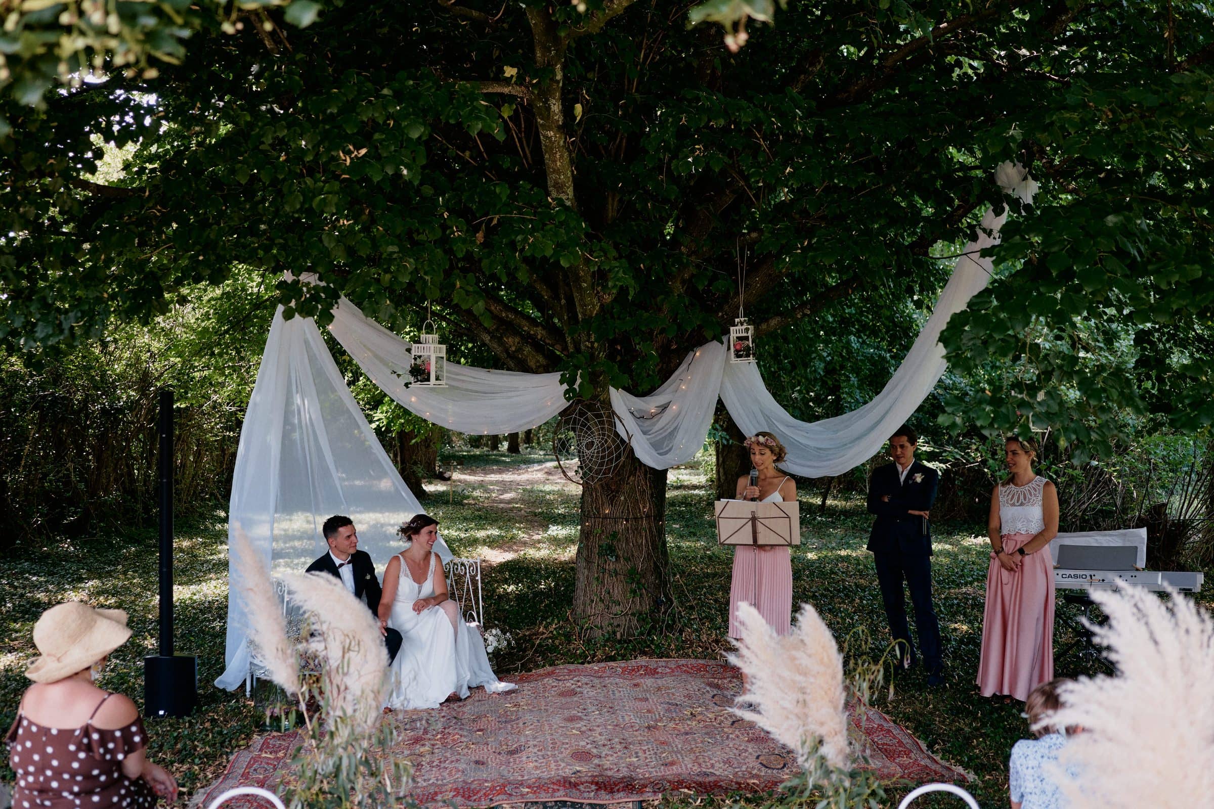 Celebrant-led ceremony beneath a tree, with drapes and a discreet speaker