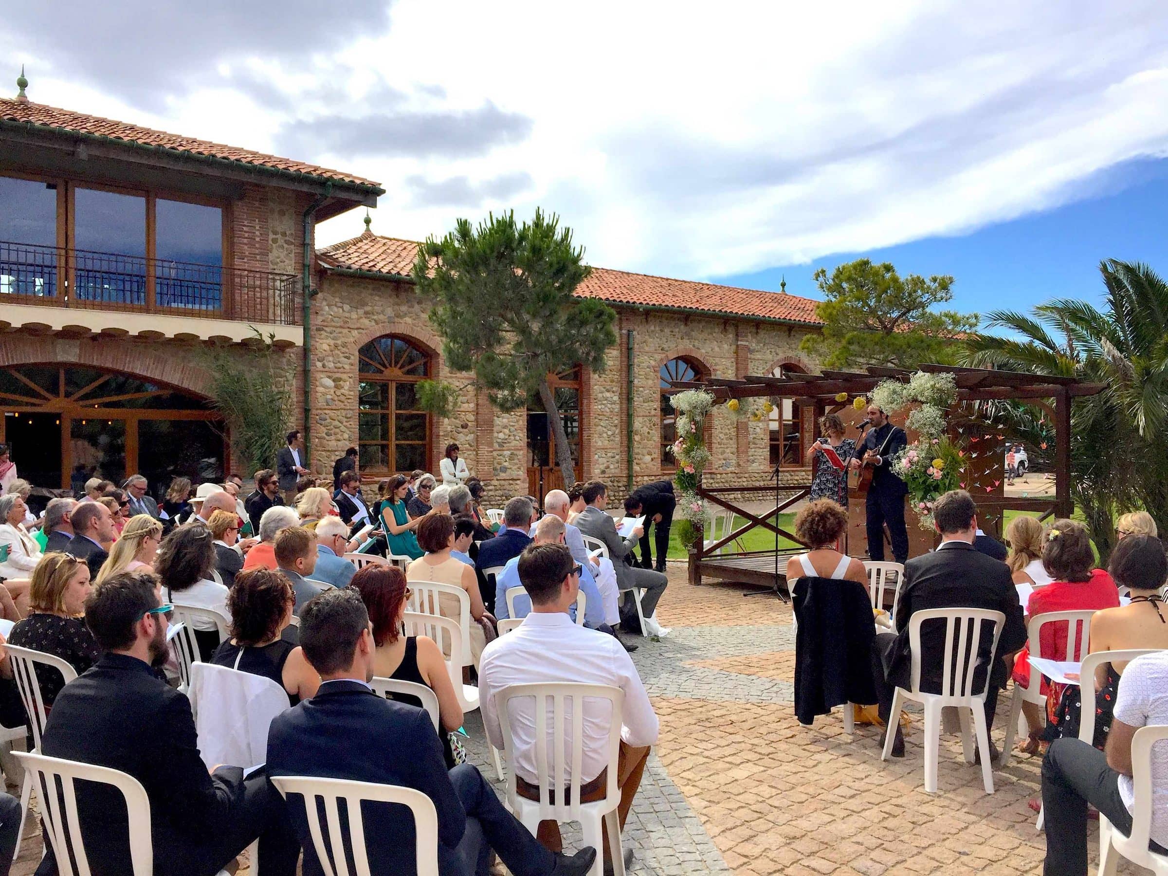 Celebrant-led ceremony in a sunny courtyard, guests seated facing the musicians