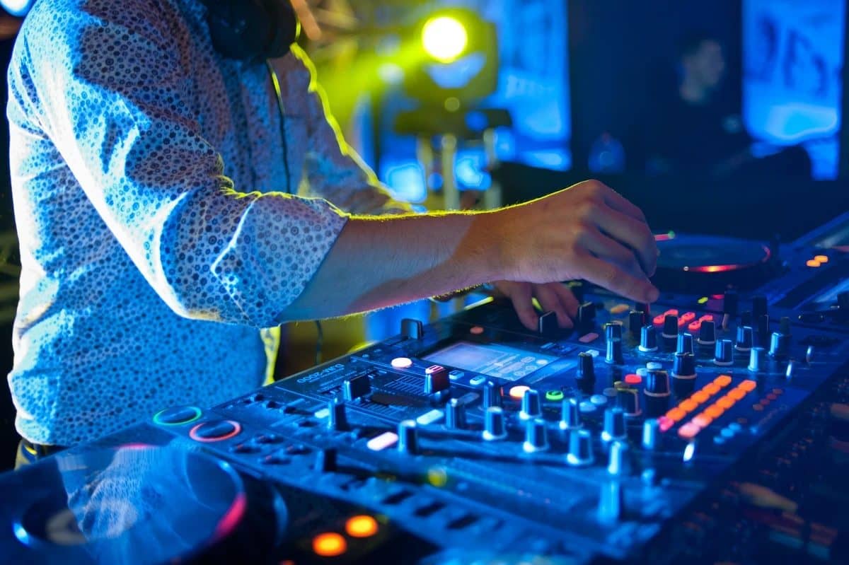 Mains d'un DJ sur une table de mixage éclairée en bleu
