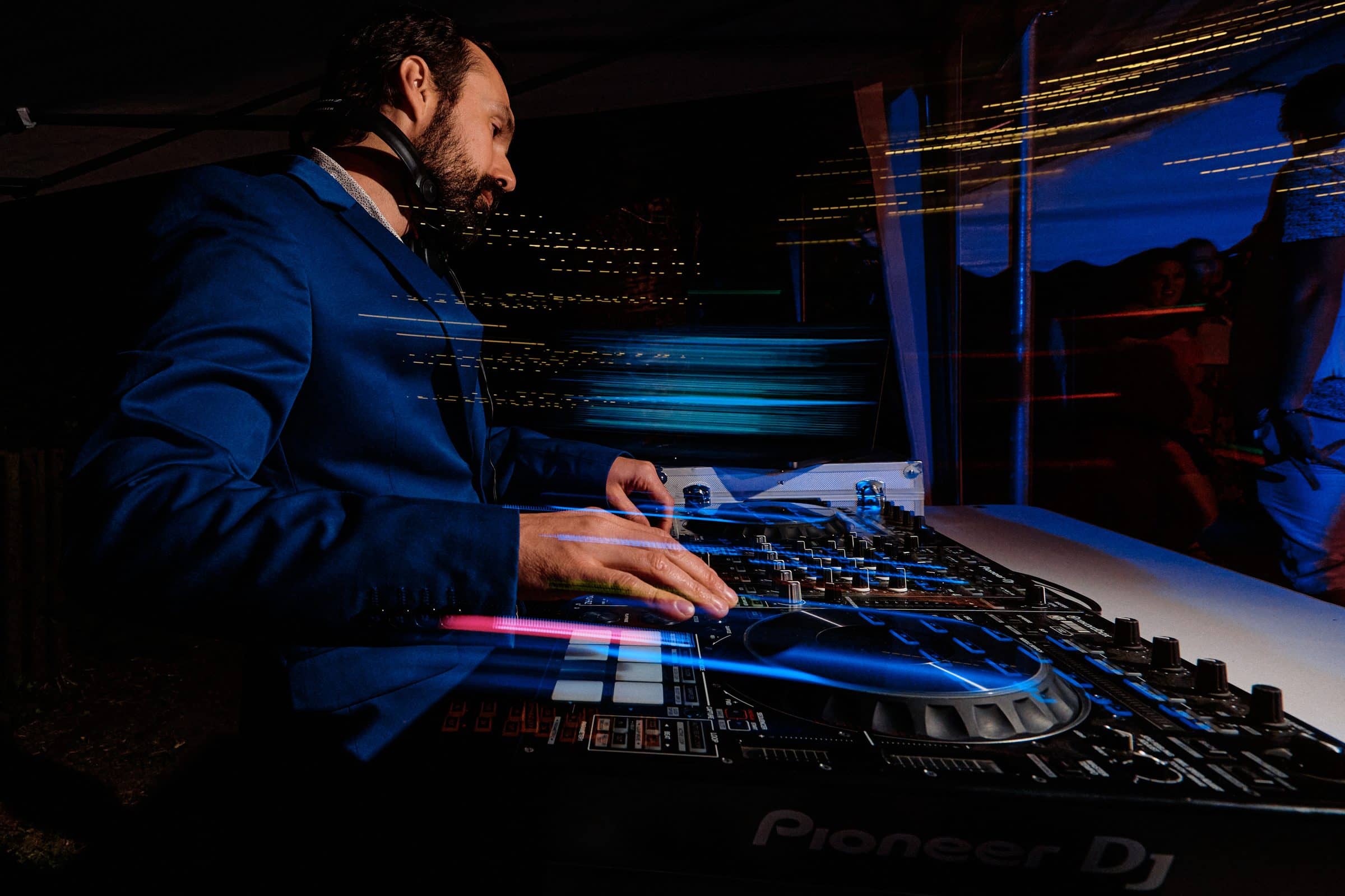 DJ at the decks, hands on the mixer, under light trails
