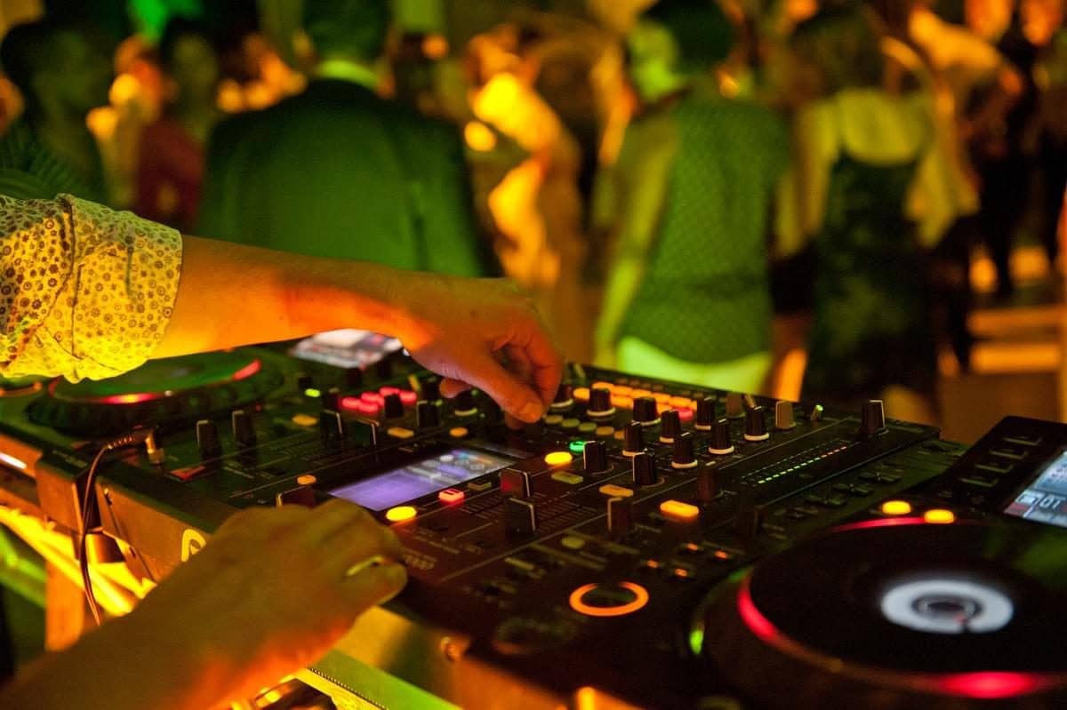 Mains d'un DJ sur les platines, piste de danse en arrière-plan