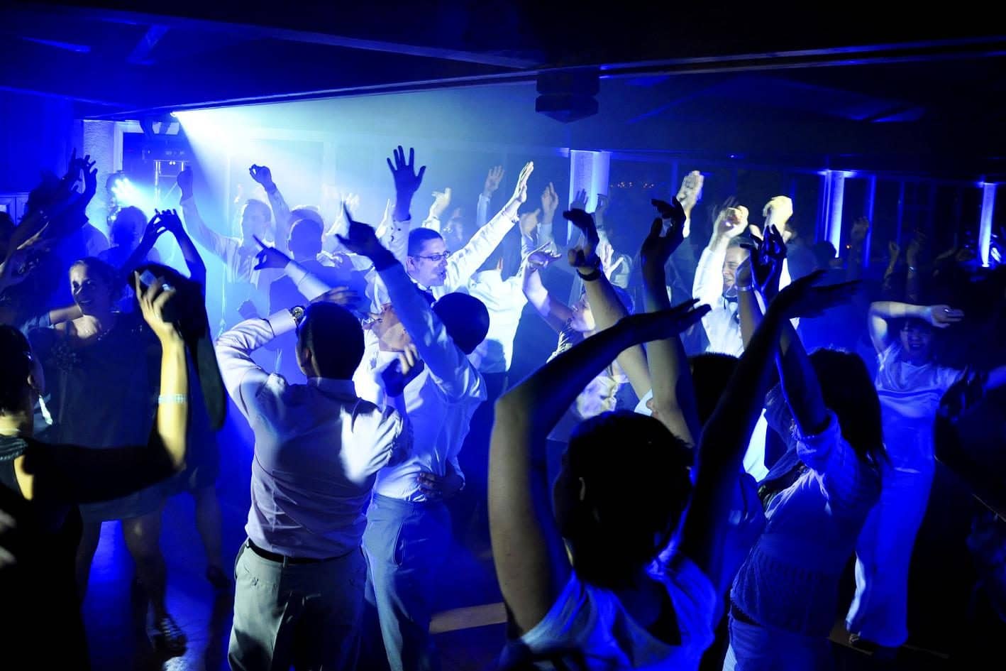 Guests with their arms in the air on a blue-lit dance floor