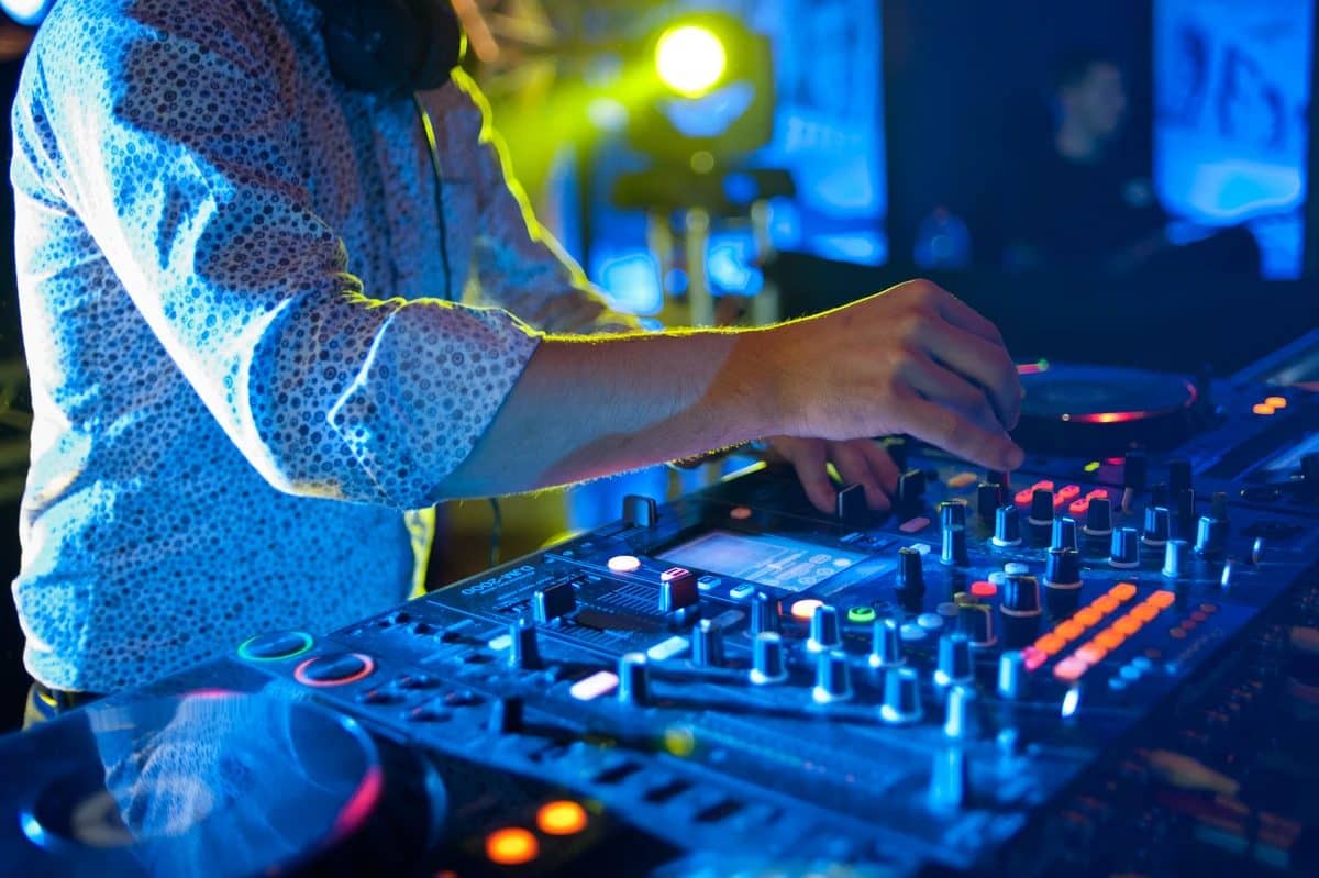 Mains d'un DJ sur une table de mixage éclairée en bleu